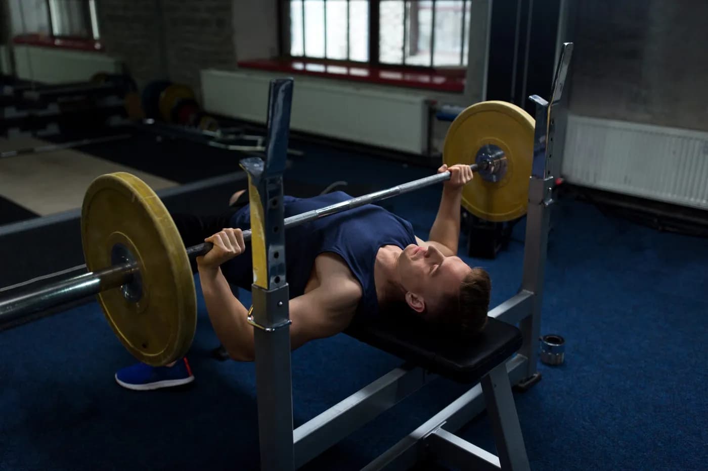 Man flexing muscles with a barbell in the gym, illustrating the benefits of the bench press