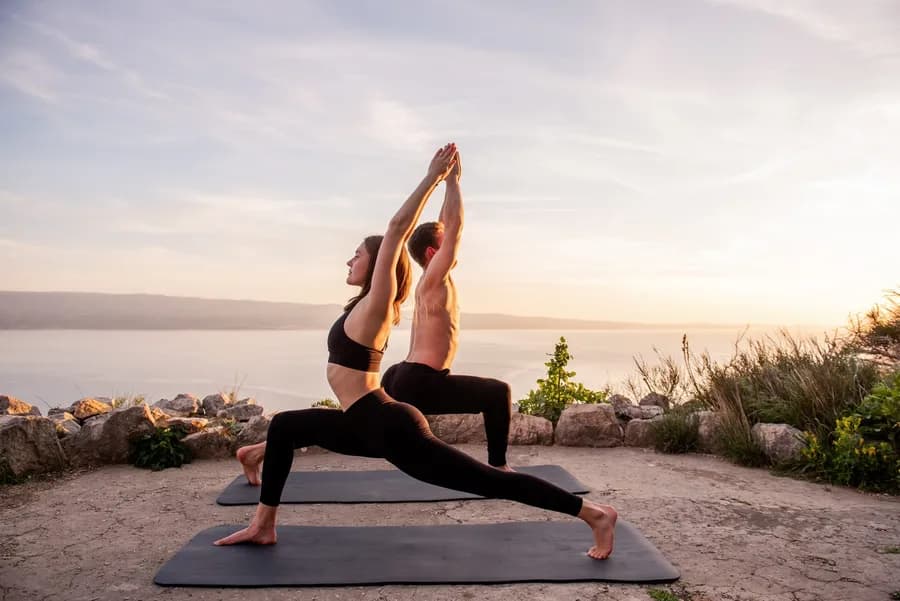 Couple doing yoga warrior pose at sunset