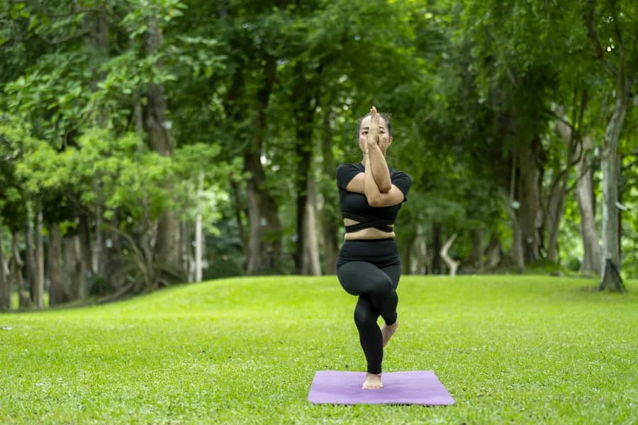 Woman practicing eagle pose (Garudasana) balance stretch outdoors in a park