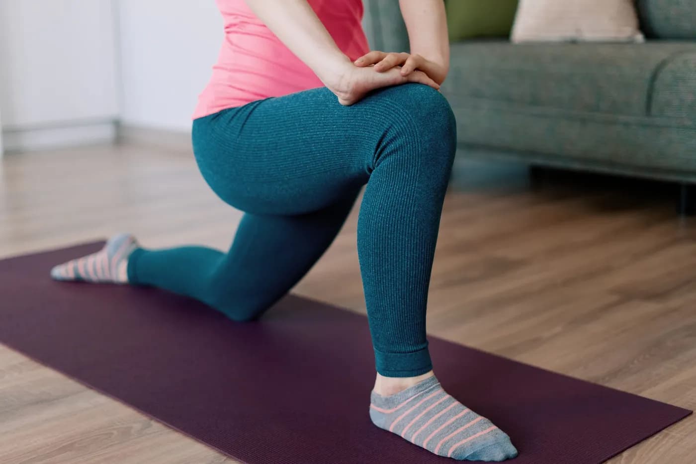 Woman stretching her leg for hip pain relief on an exercise mat indoors