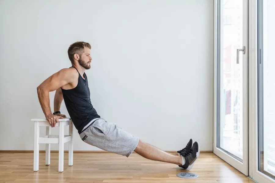 Man exercising at home using a chair for triceps dips as part of a no equipment strength workout