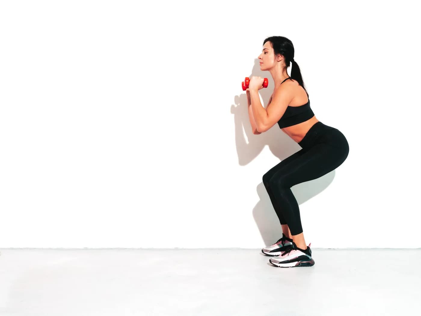Woman doing squats with dumbbells in a fitness studio