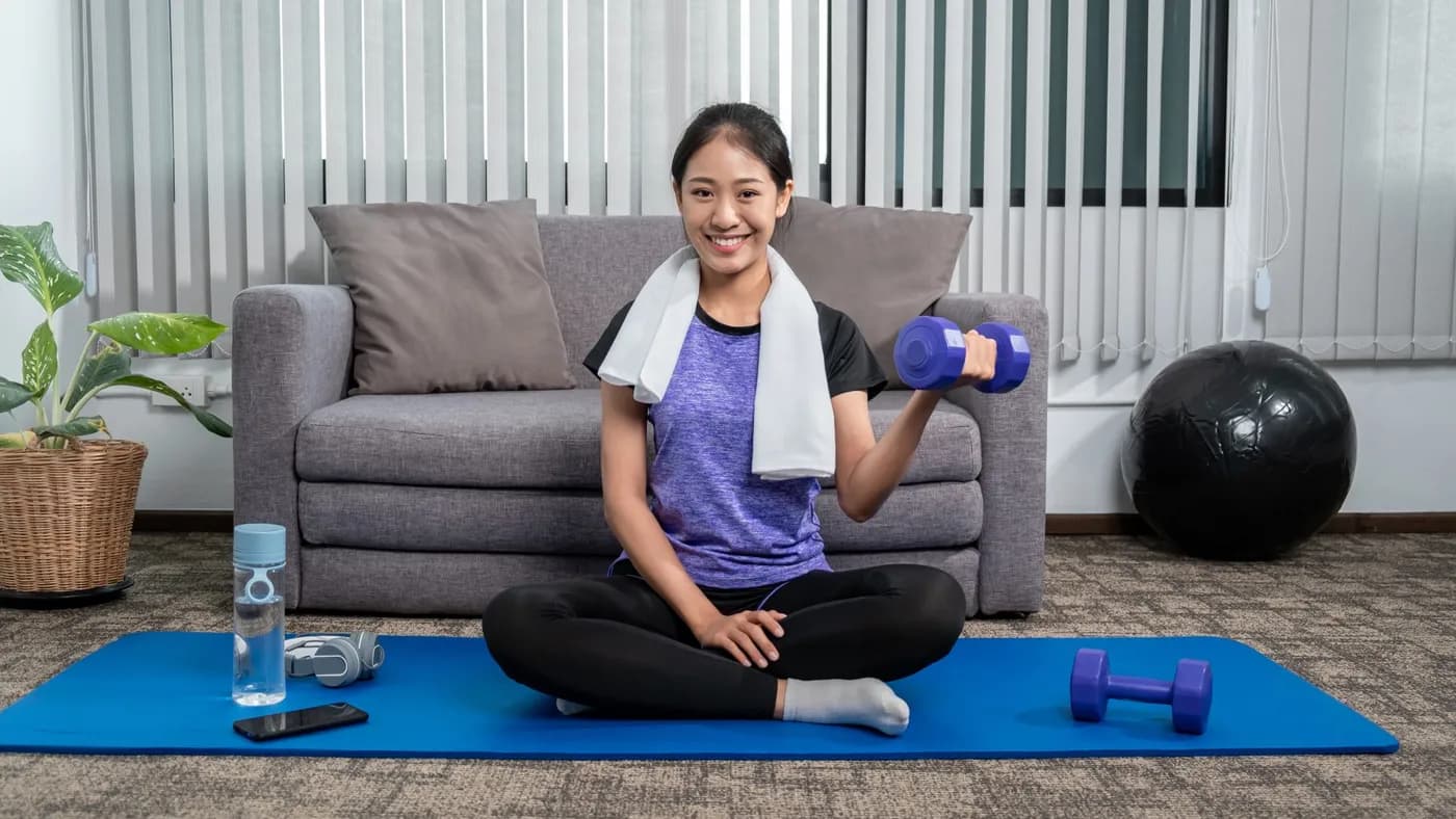 Smiling woman lifting weights at home on a yoga mat during a strength training workout