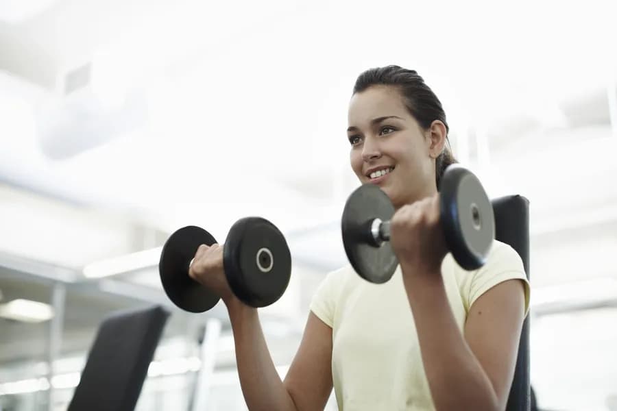 Smiling woman lifting dumbbells in a gym during a beginner strength training workout