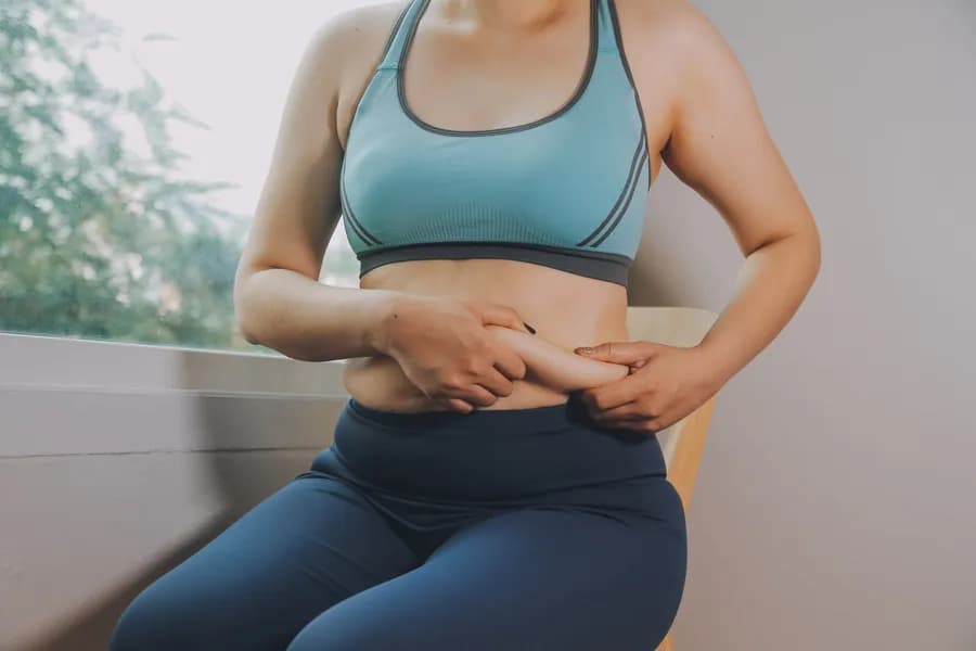 Woman holding her belly fat, illustrating the topic of exercises to reduce belly fat