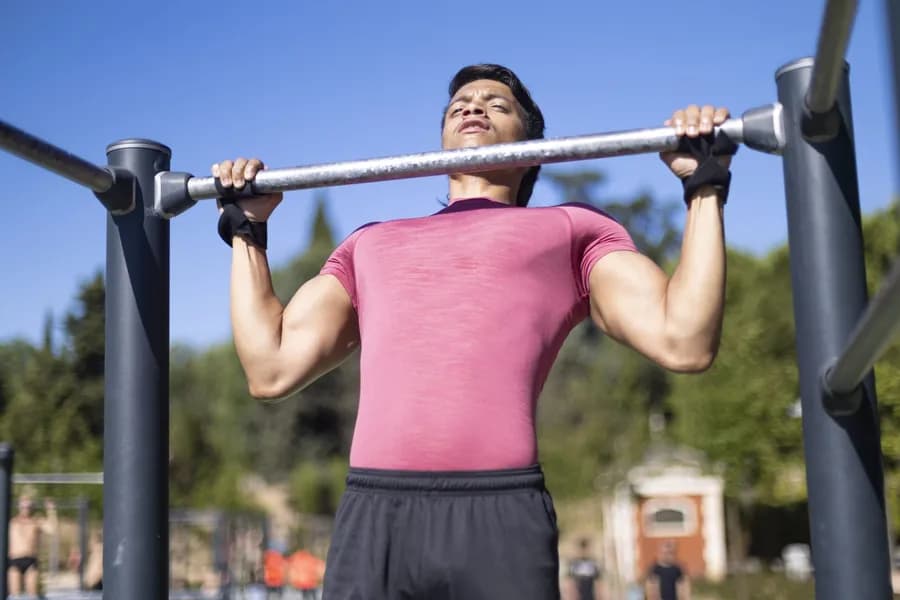 Man in a pink shirt doing pull ups on outdoor gym equipment