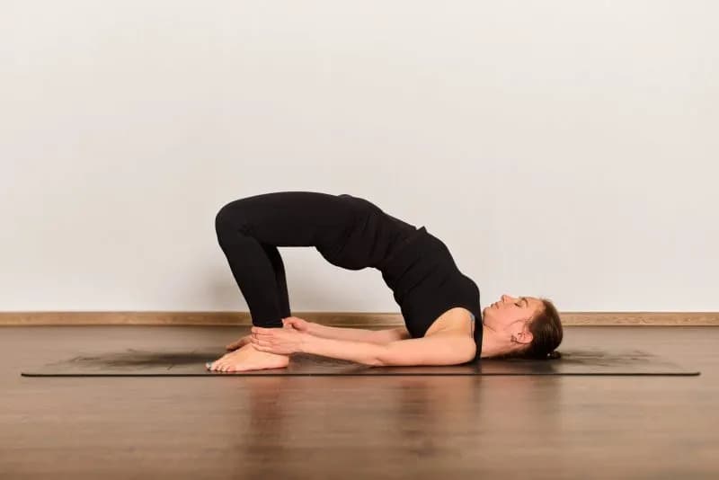 woman performing Setubandhasana yoga pose, lying on back with hips lifted and feet on the mat
